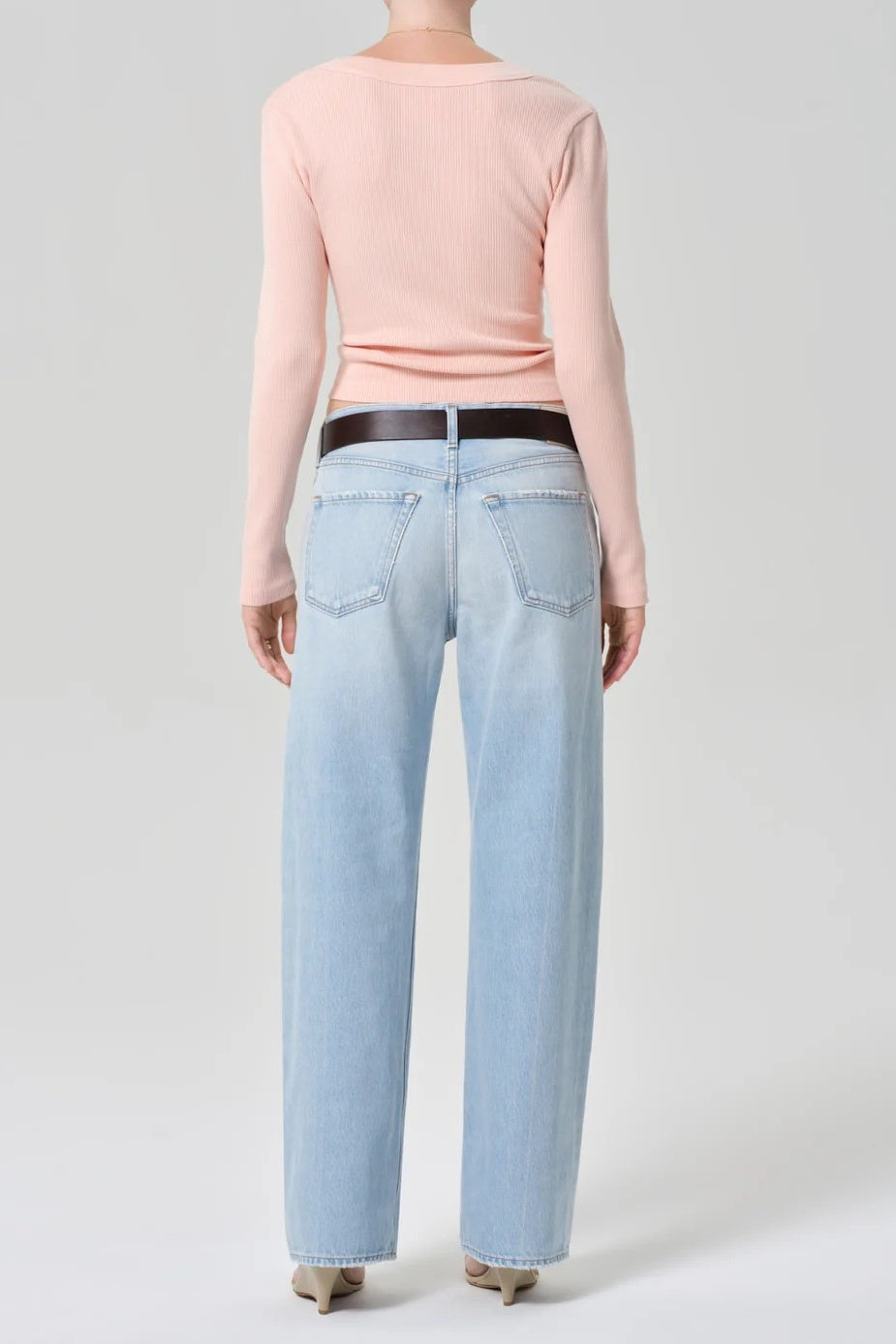 Person wearing light blue jeans and a pink top on a plain background