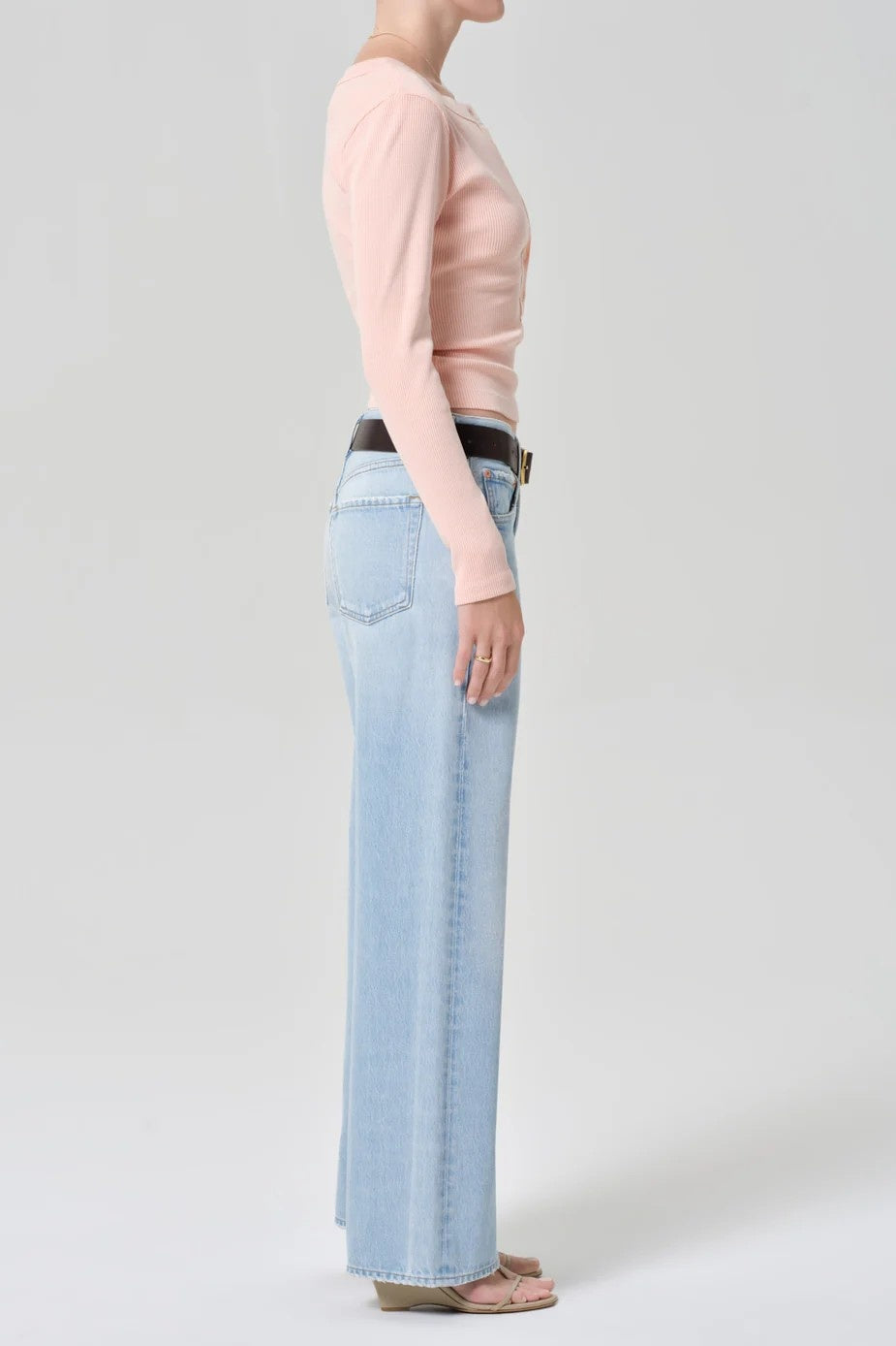 Person wearing a light pink long-sleeve top and light blue jeans on a plain background