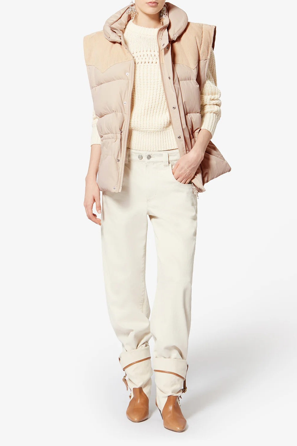 Person wearing a light beige puffer vest over a cream sweater and pants on a white background