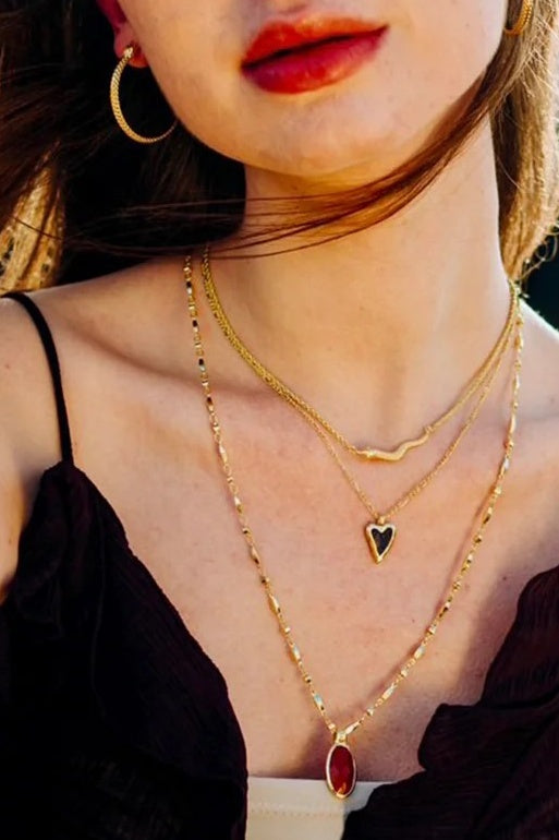 Close-up of a person wearing gold necklaces with heart and red pendant  and snake designs.