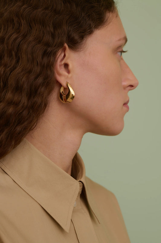 Close-up of a person wearing gold hoop earrings with a neutral background