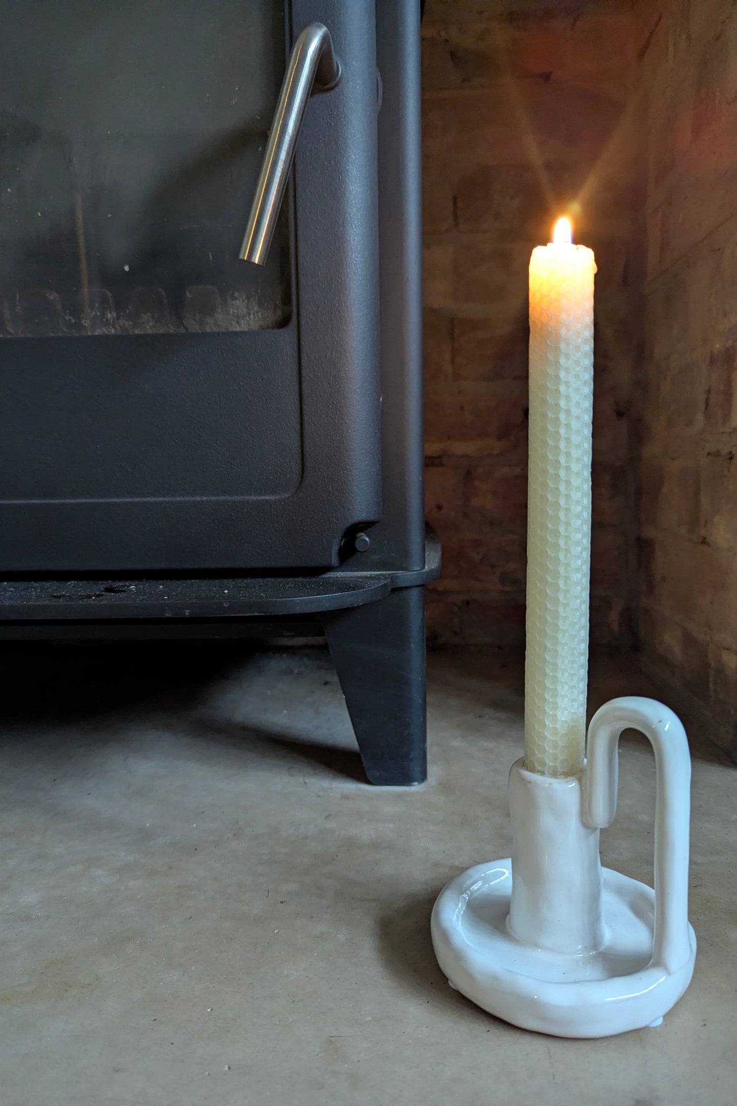 Candle in a white holder next to a black stove with a wooden wall background