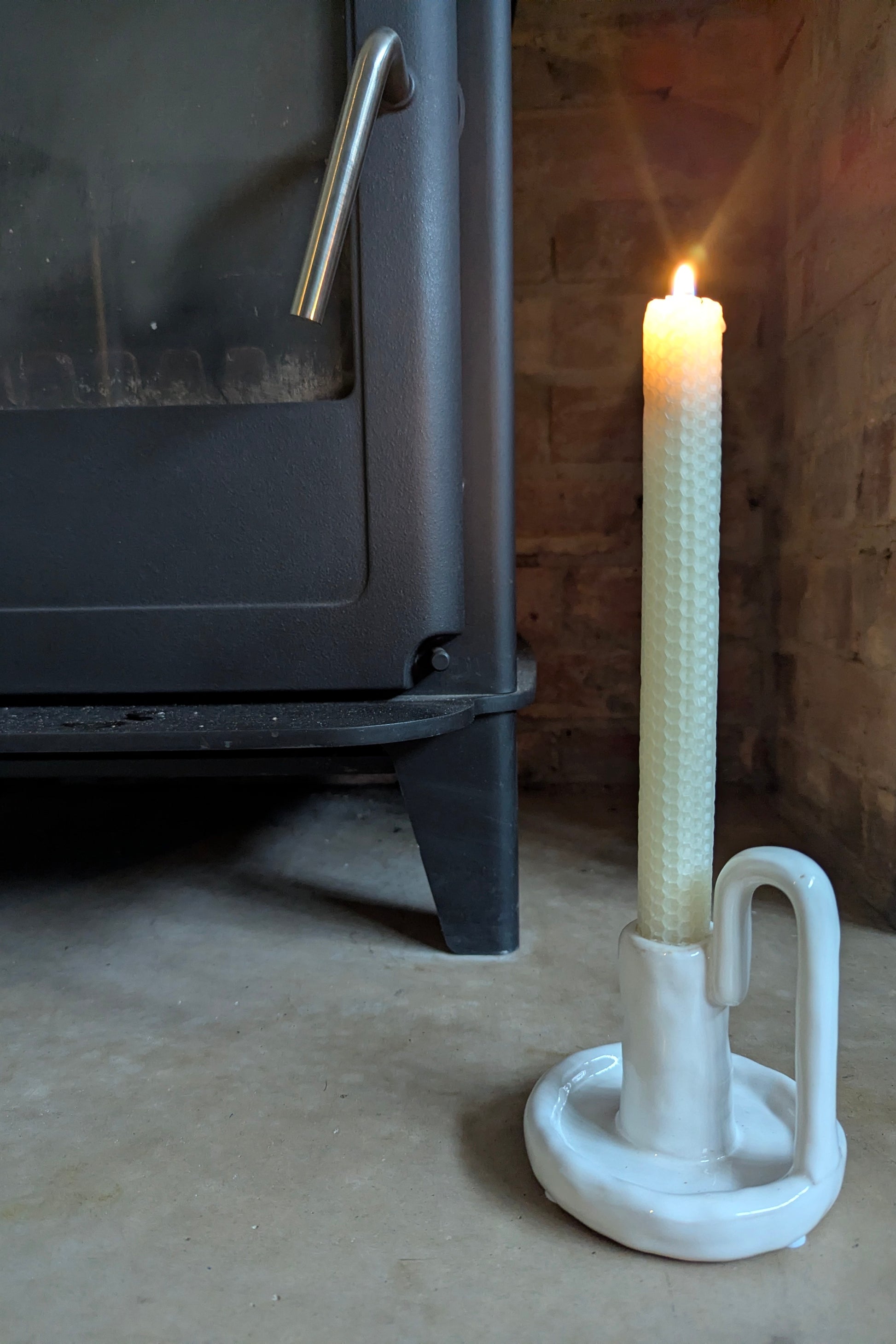 Candle in a white holder next to a black stove with a wooden wall background