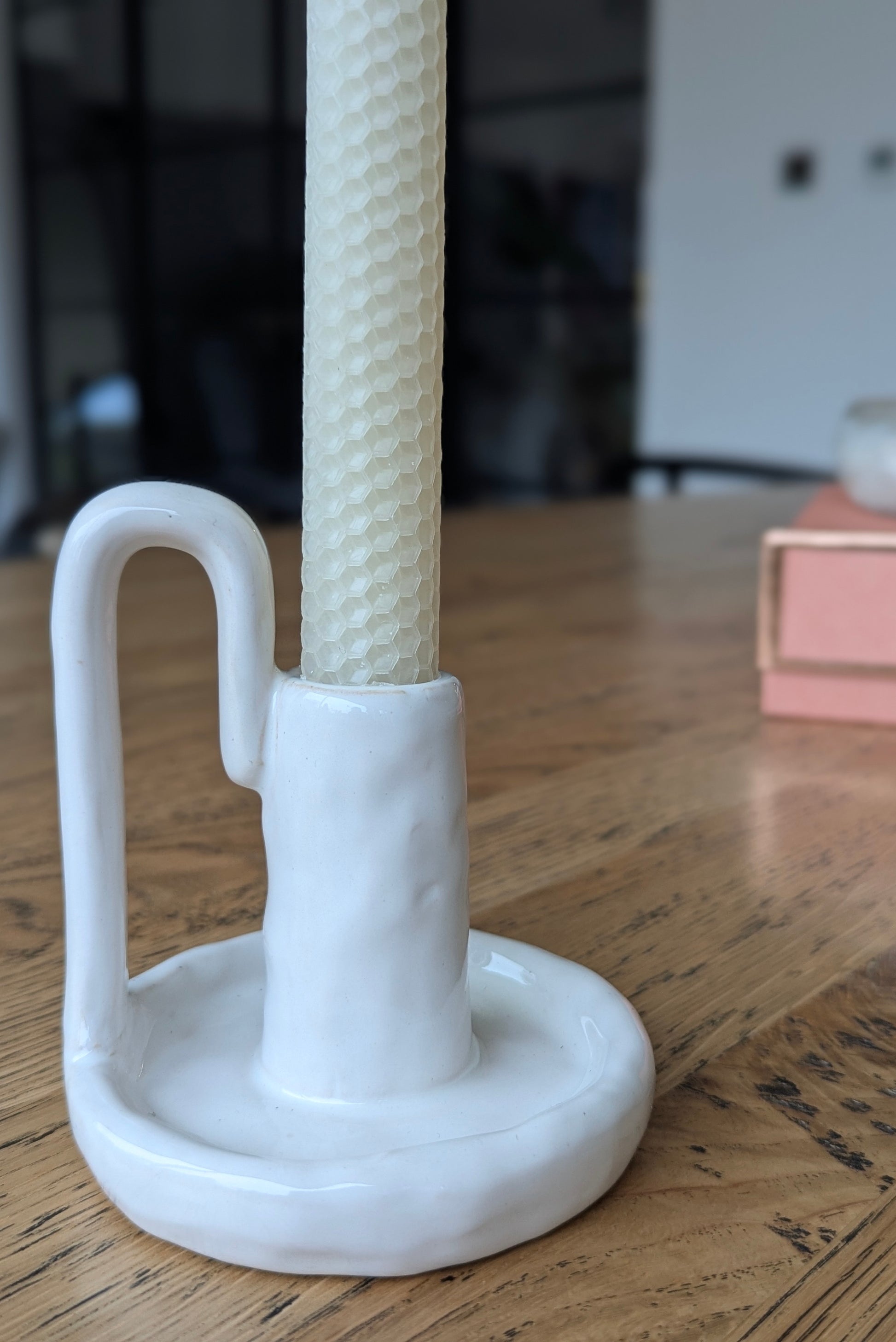 White ceramic holder with a textured white candle on a wooden surface