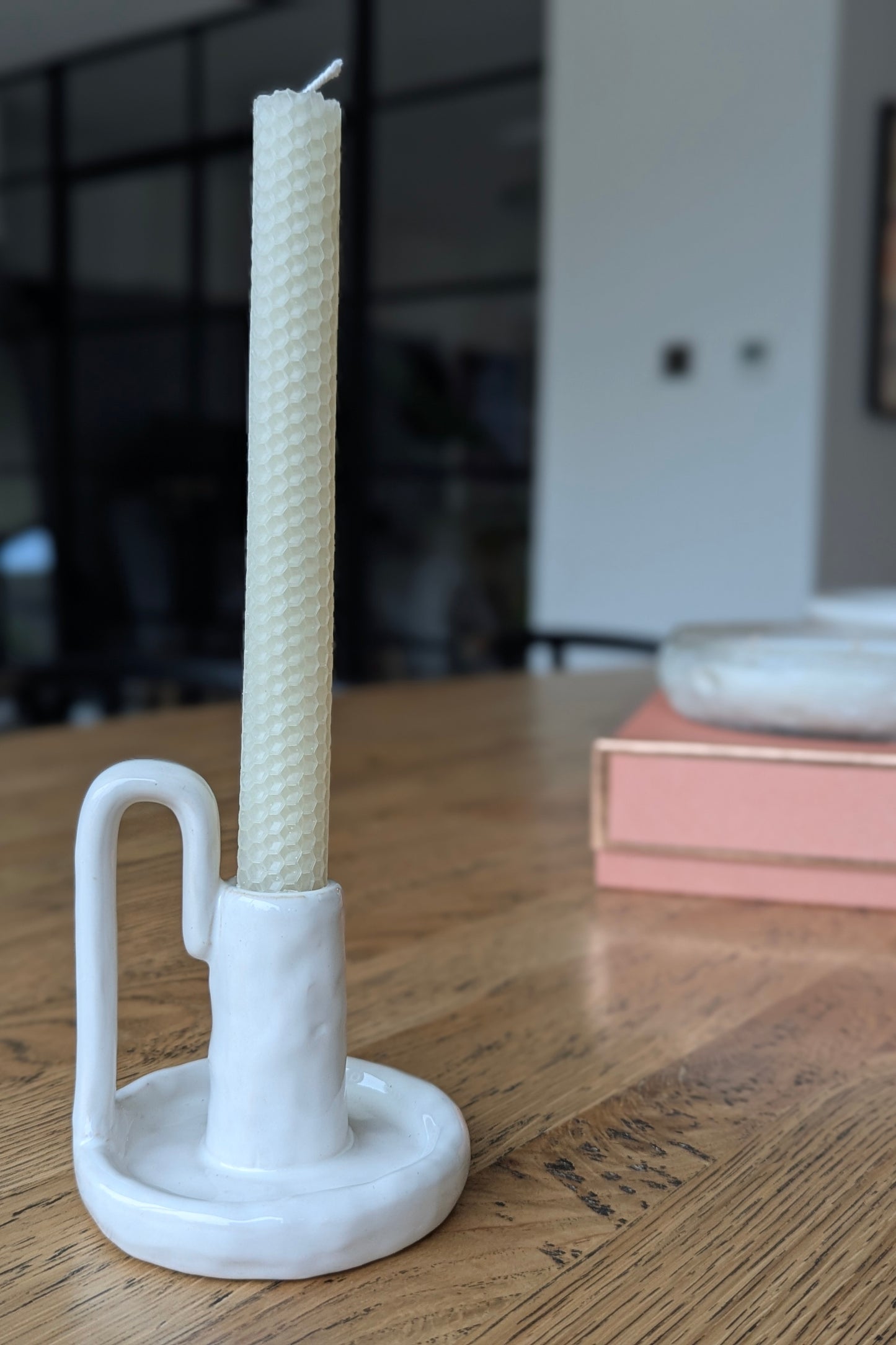 White candle holder with a candle on a wooden surface