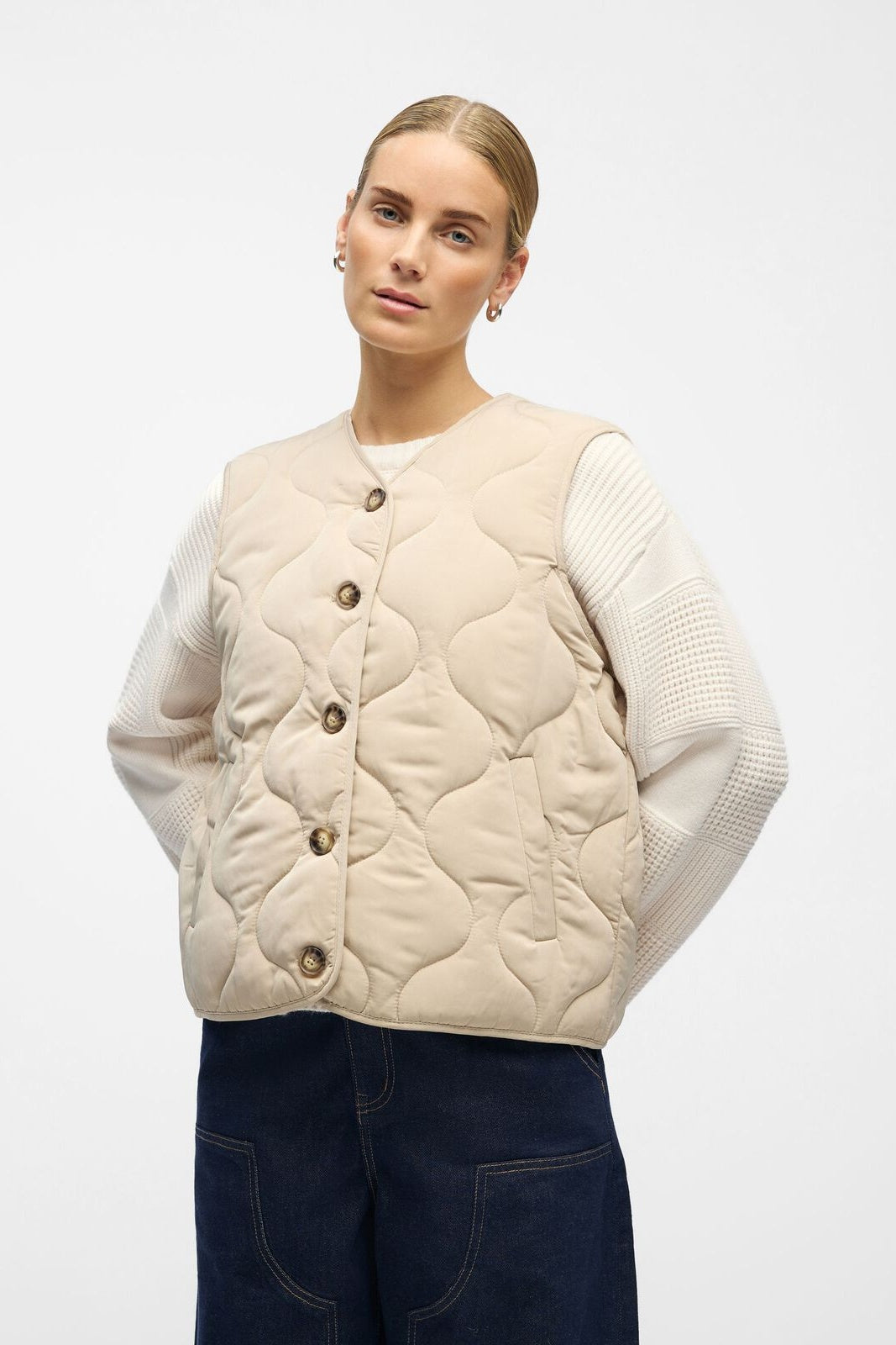 Woman wearing a beige quilted vest over a white sweater on a white background