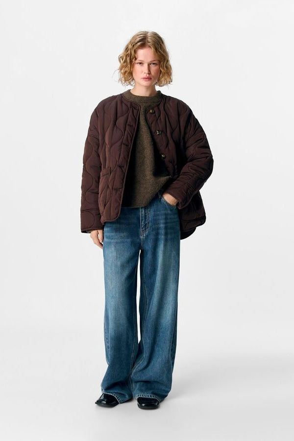 Person wearing a brown quilted jacket and blue jeans on a white background