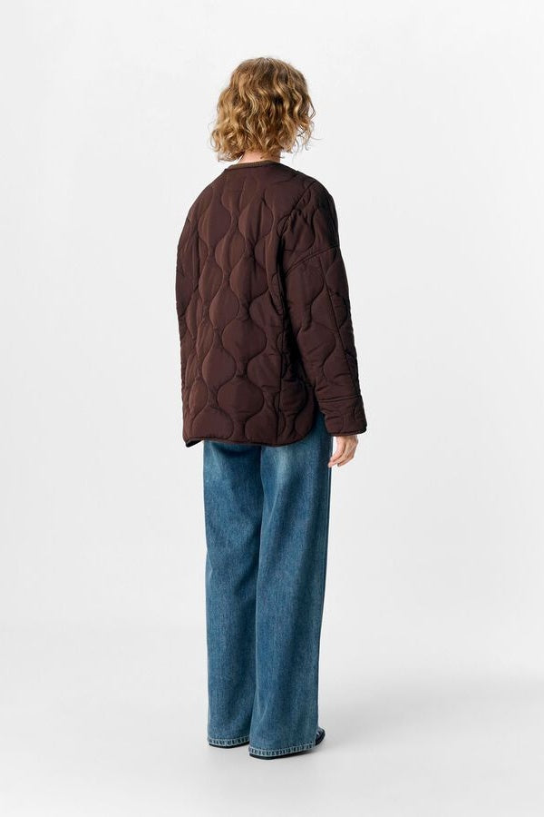 Person wearing a brown quilted jacket and blue jeans on a white background