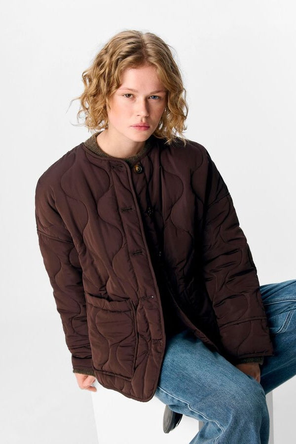 Person wearing a brown quilted jacket and blue jeans on a white background