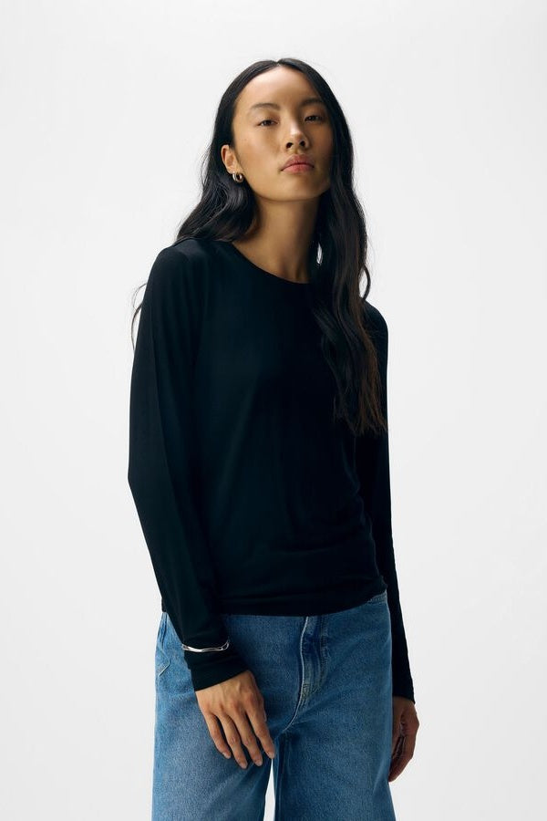 Woman wearing a black long-sleeve top and blue jeans on a white background