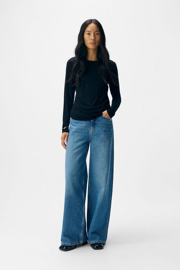 Woman wearing a black long-sleeve top and blue jeans on a white background