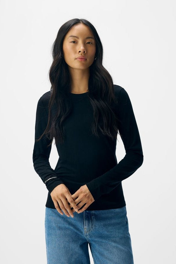 Woman wearing a black long-sleeve top and blue jeans on a white background