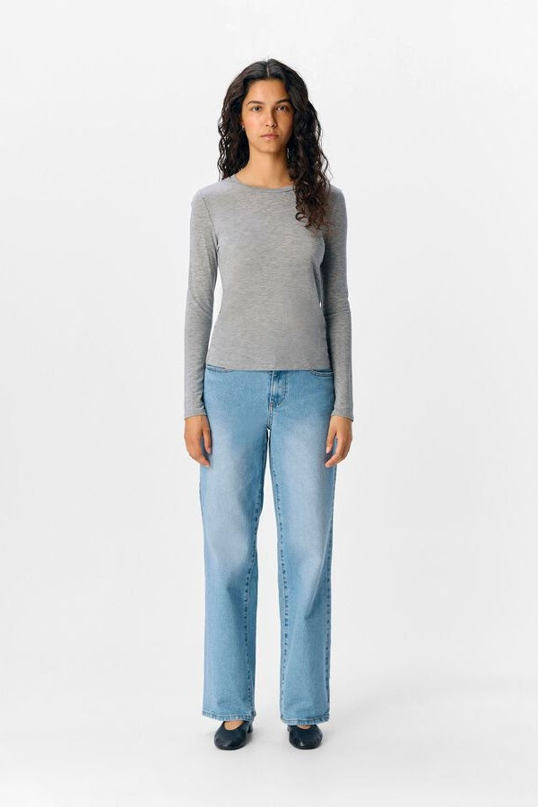 Woman wearing a grey long sleeve tshirt and light blue jeans on a white background