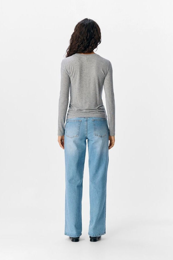 Person wearing a grey long-sleeve top and light blue jeans on a white background