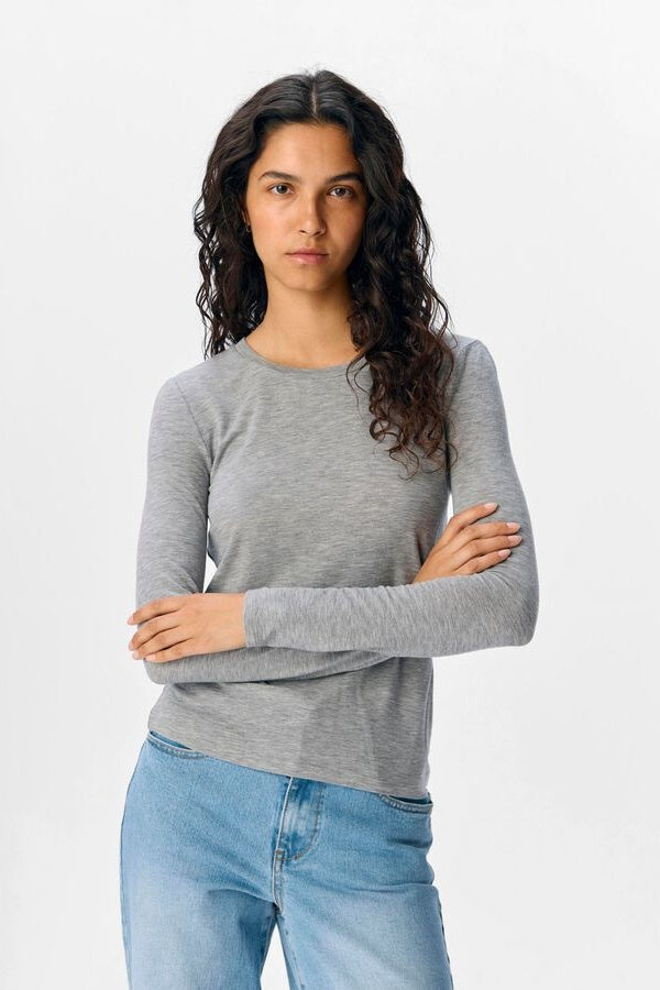 Woman wearing a grey long-sleeve shirt and blue jeans on a white background