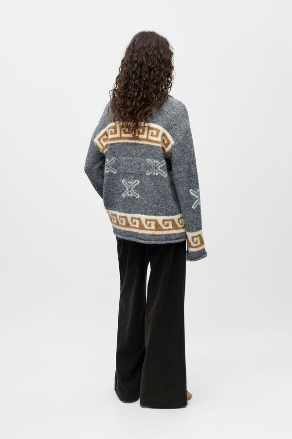 Person wearing a grey patterned sweater with a plain background