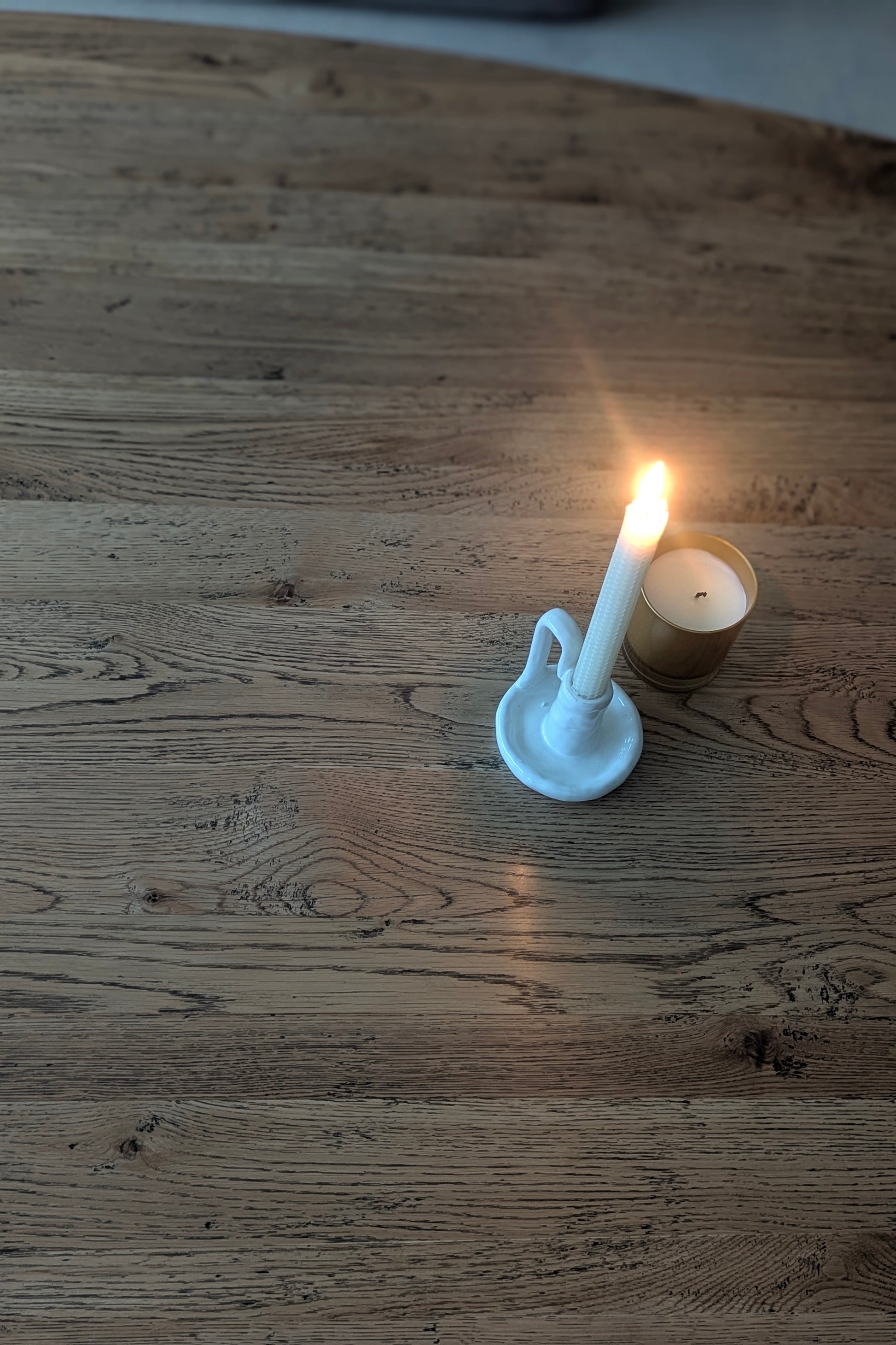 Candle in a white holder on a wooden surface