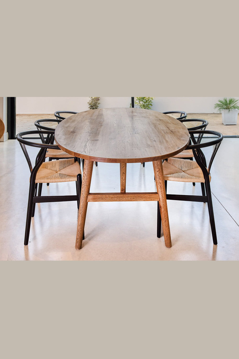 Oval wooden dining table with black chairs in a minimalistic setting