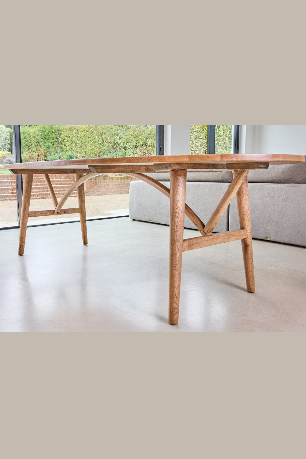 Wooden dining table in a modern living room with a sofa and large windows.