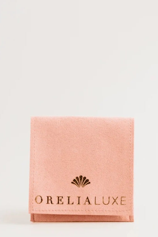Pink jewelry pouch with 'OreliaLuxe' logo on a light gray background