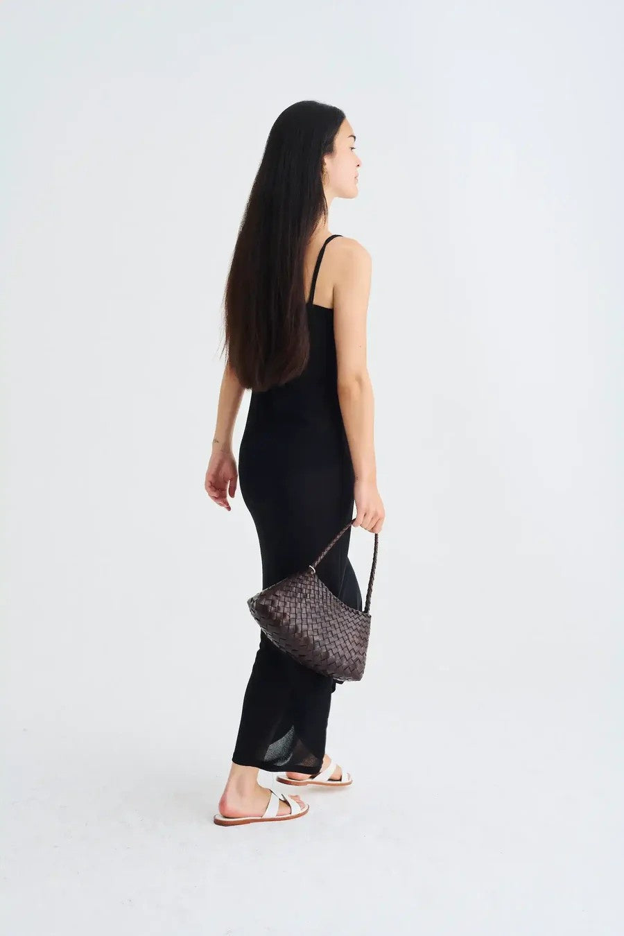 Woman in a black dress holding a textured handbag on a white background