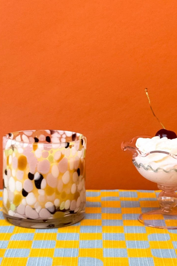 Decorative glass vase with floral pattern on a checkered tablecloth against an orange wall.