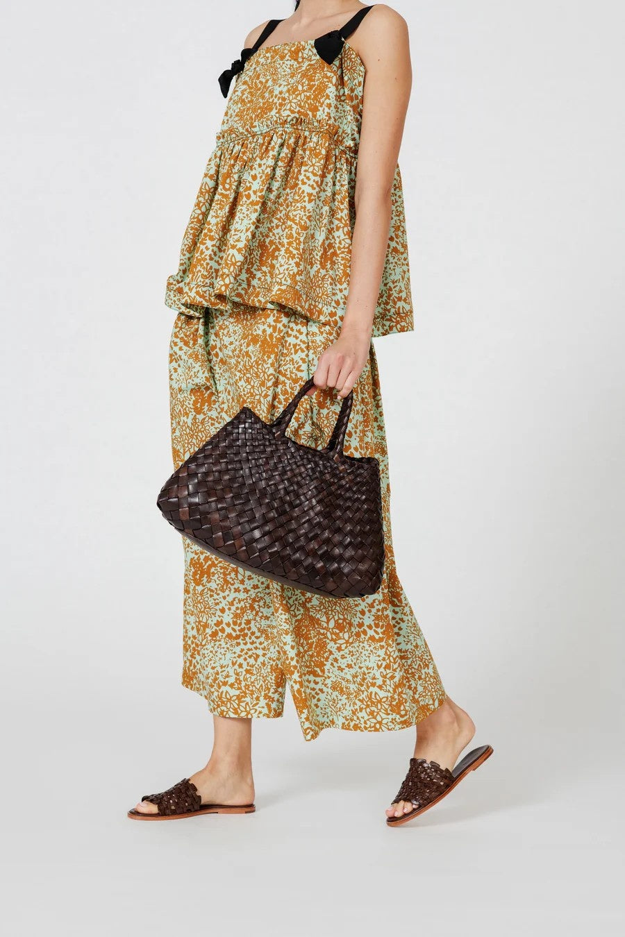Woman in a floral dress holding a woven handbag on a white background