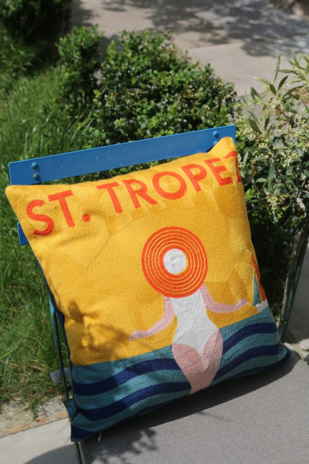 Colorful pillow with 'ST. TROPEZ' text on a chair outdoors