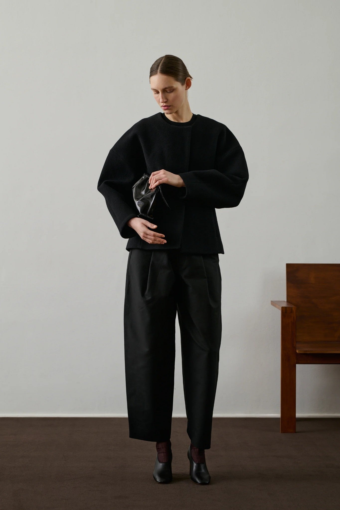 Person wearing a black outfit holding a black bag against a plain background