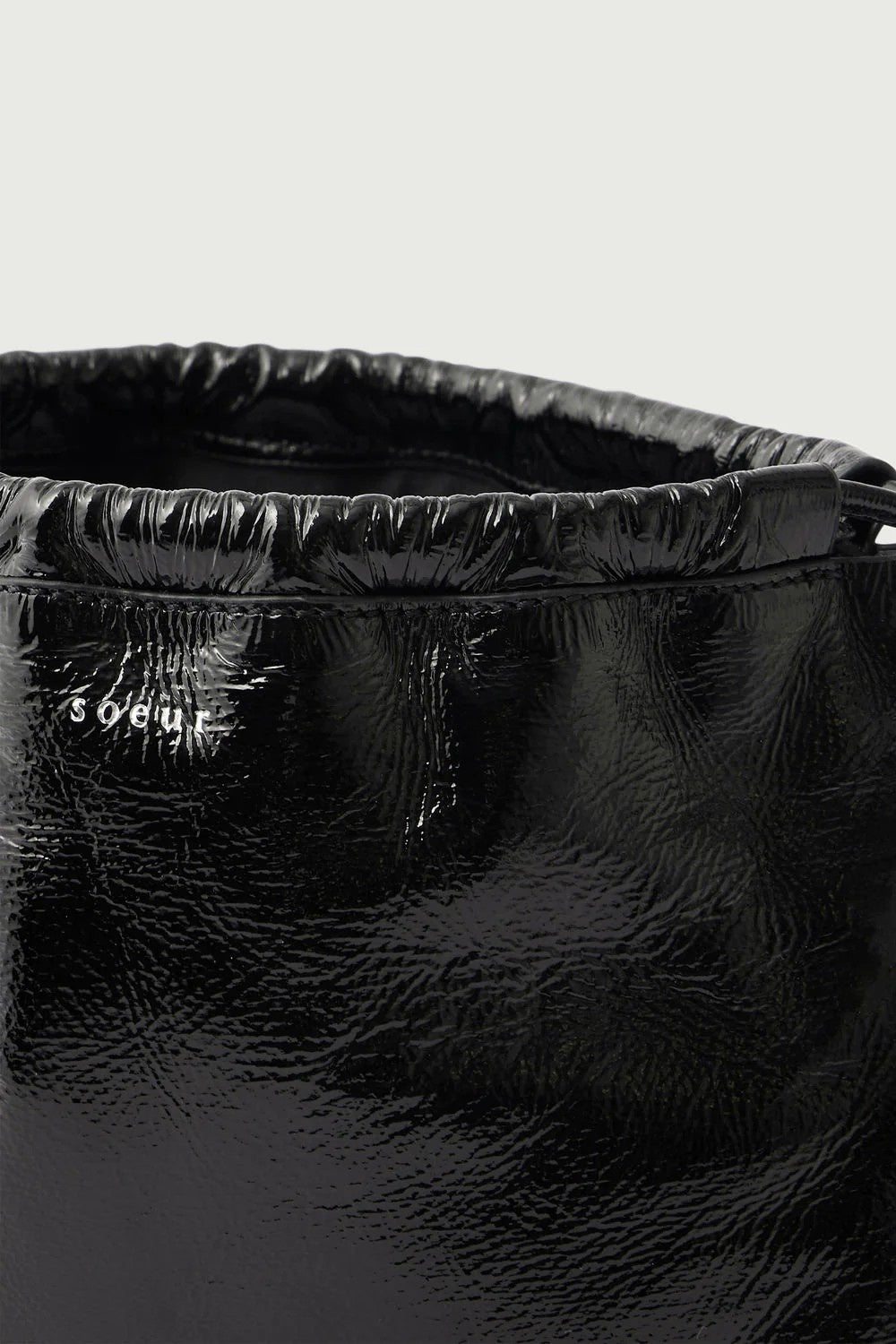 Close-up of a black pouch bag with 'Soeur' branding on a light grey background