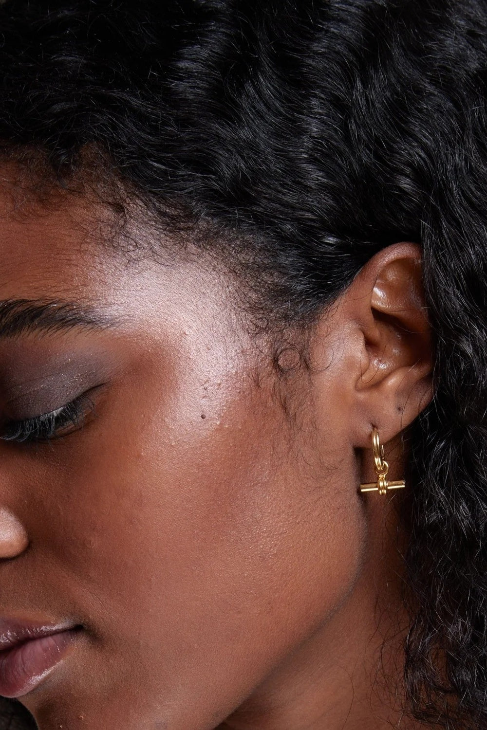 Close-up of a person wearing a gold earring with a blurred background