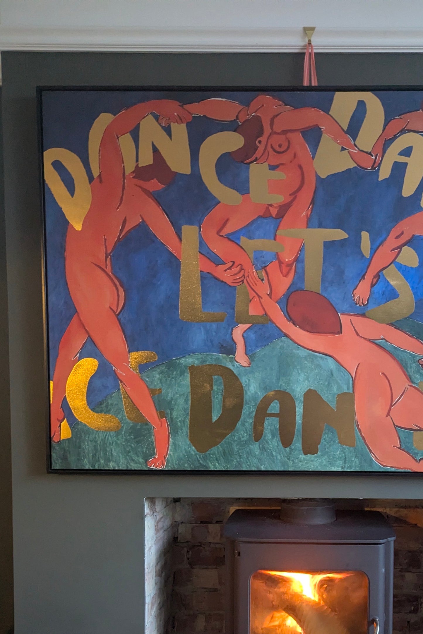 Framed artwork with dancing figures and text on a wall above a fireplace.