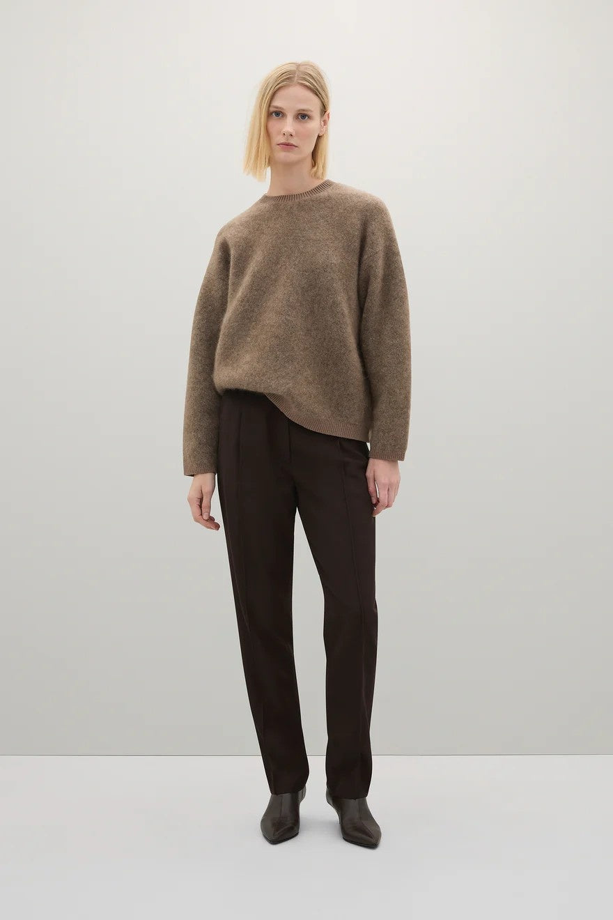 Person wearing a brown sweater and dark pants on a white background