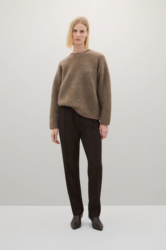 Person wearing a brown sweater and dark pants on a white background