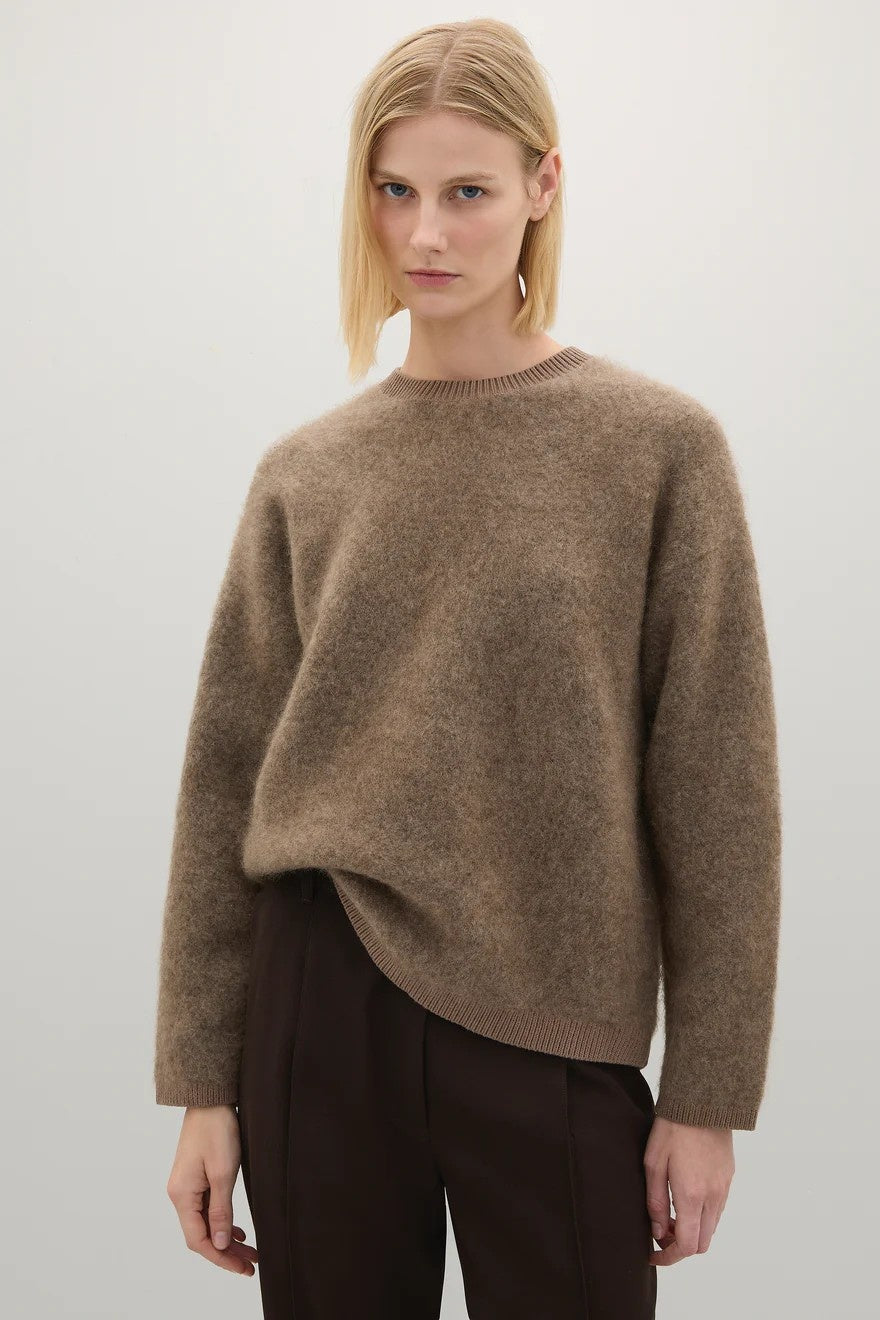 Person wearing a brown sweater and dark pants on a light gray background