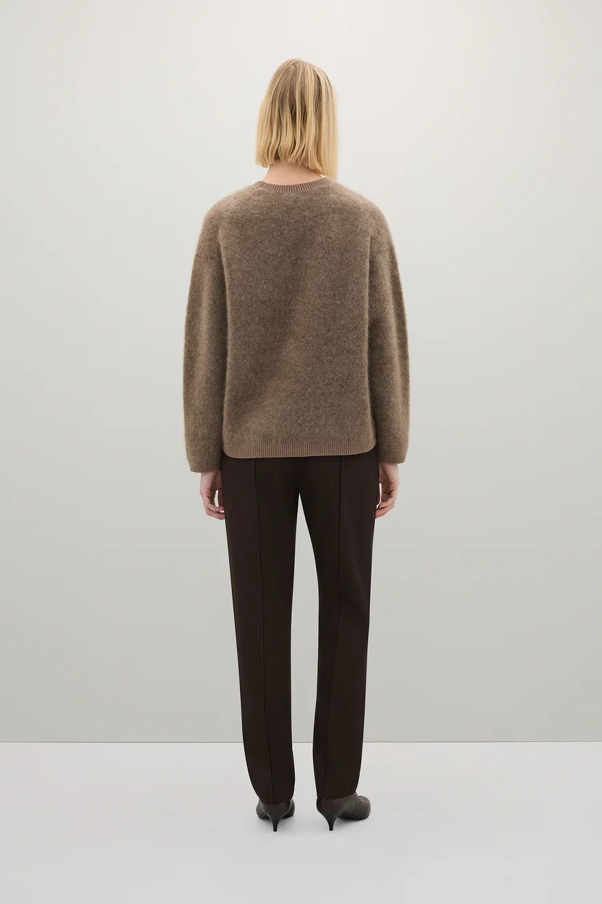 Person wearing a brown sweater and black pants on a white background