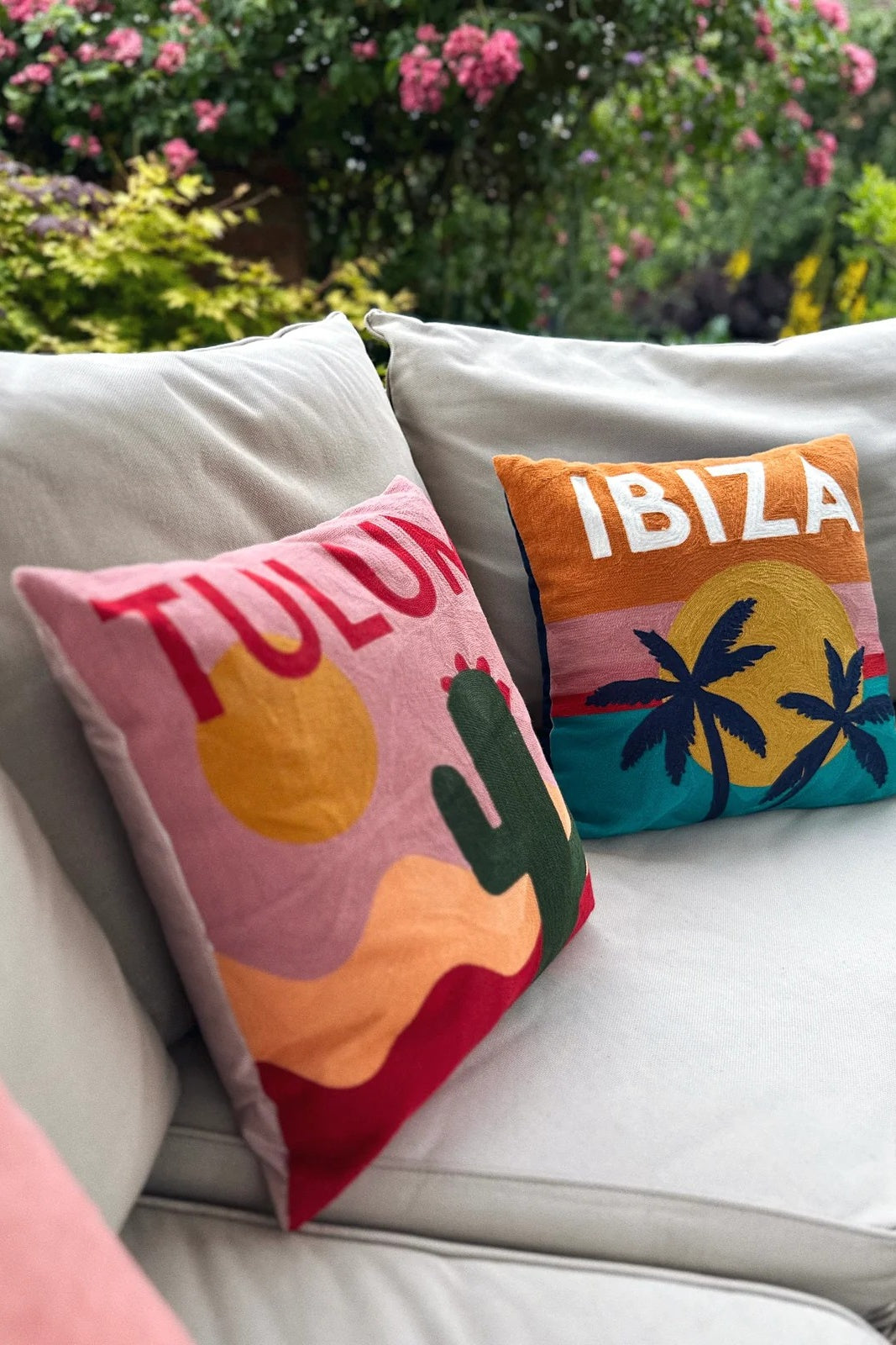 Colorful 'Tulum' and 'Ibiza' pillows on a couch with a garden background