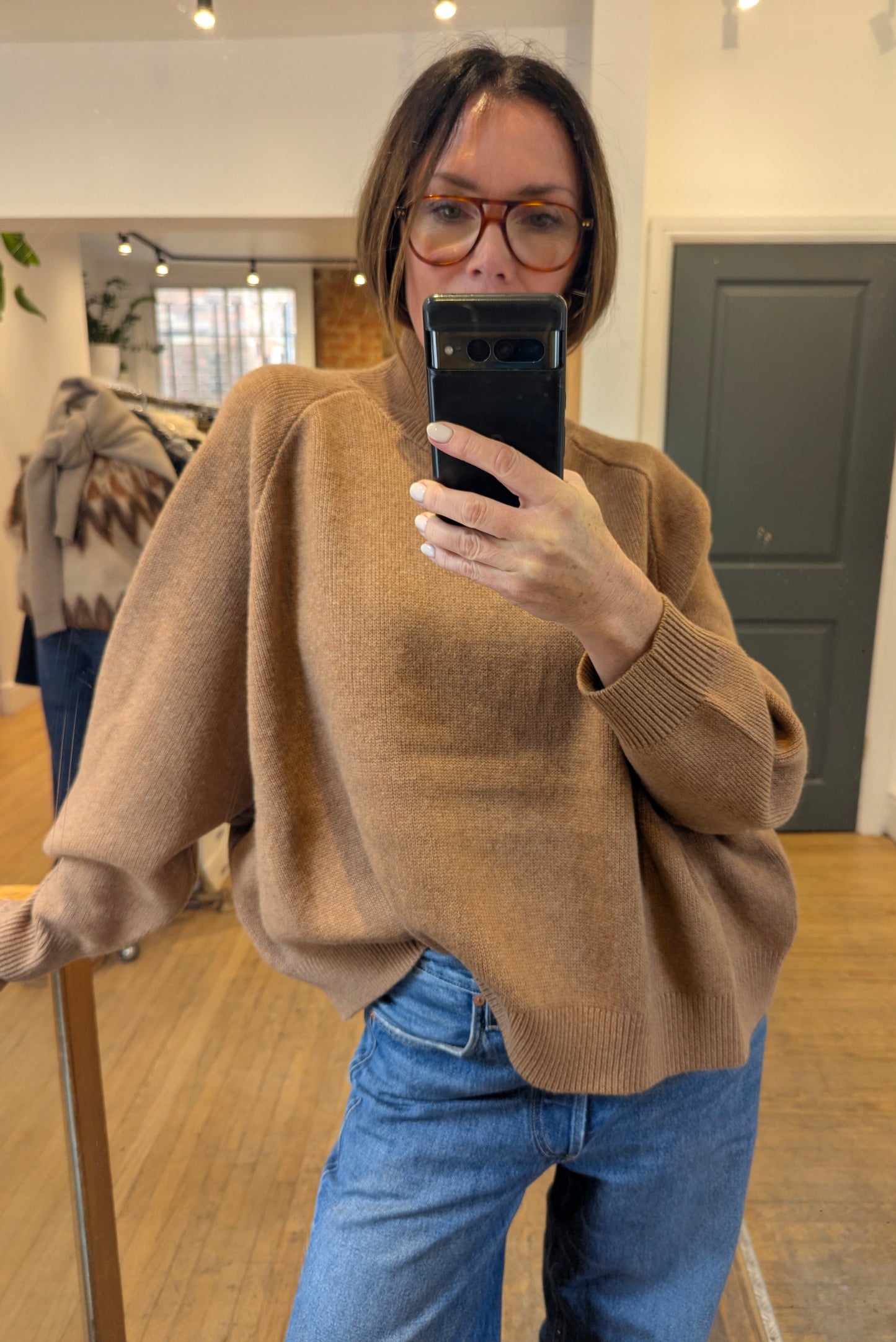 Person wearing a brown sweater and blue jeans taking a mirror selfie.