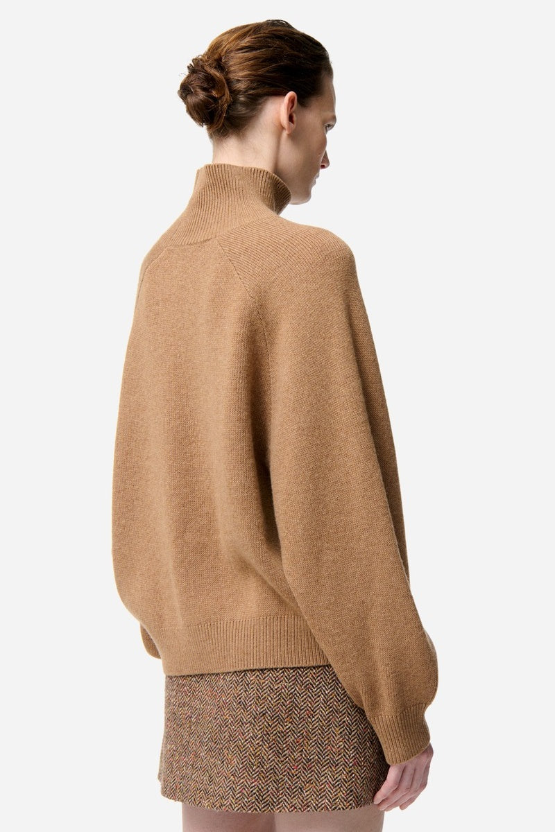 Woman wearing a beige sweater and patterned skirt on a white background