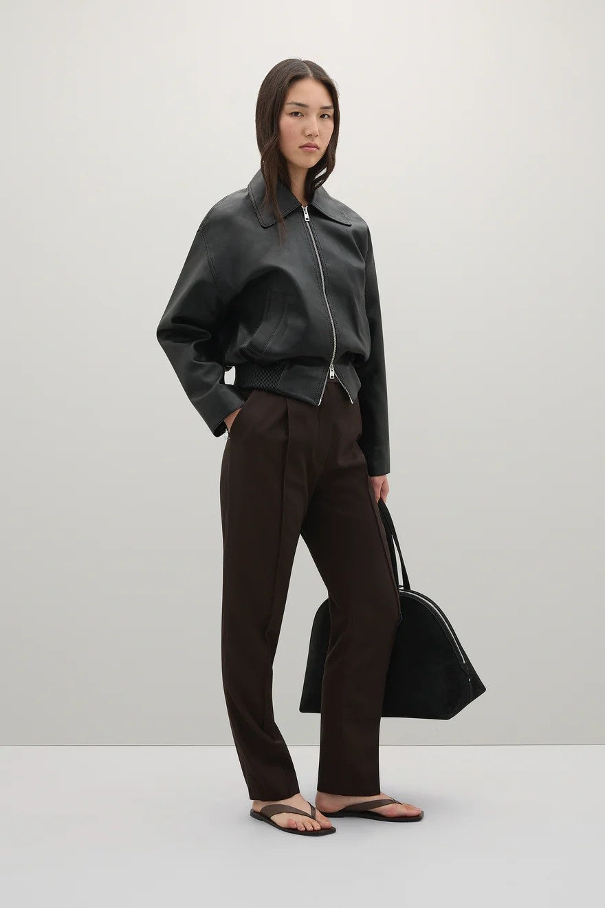 Woman wearing a black jacket and brown pants holding a black bag on a white background