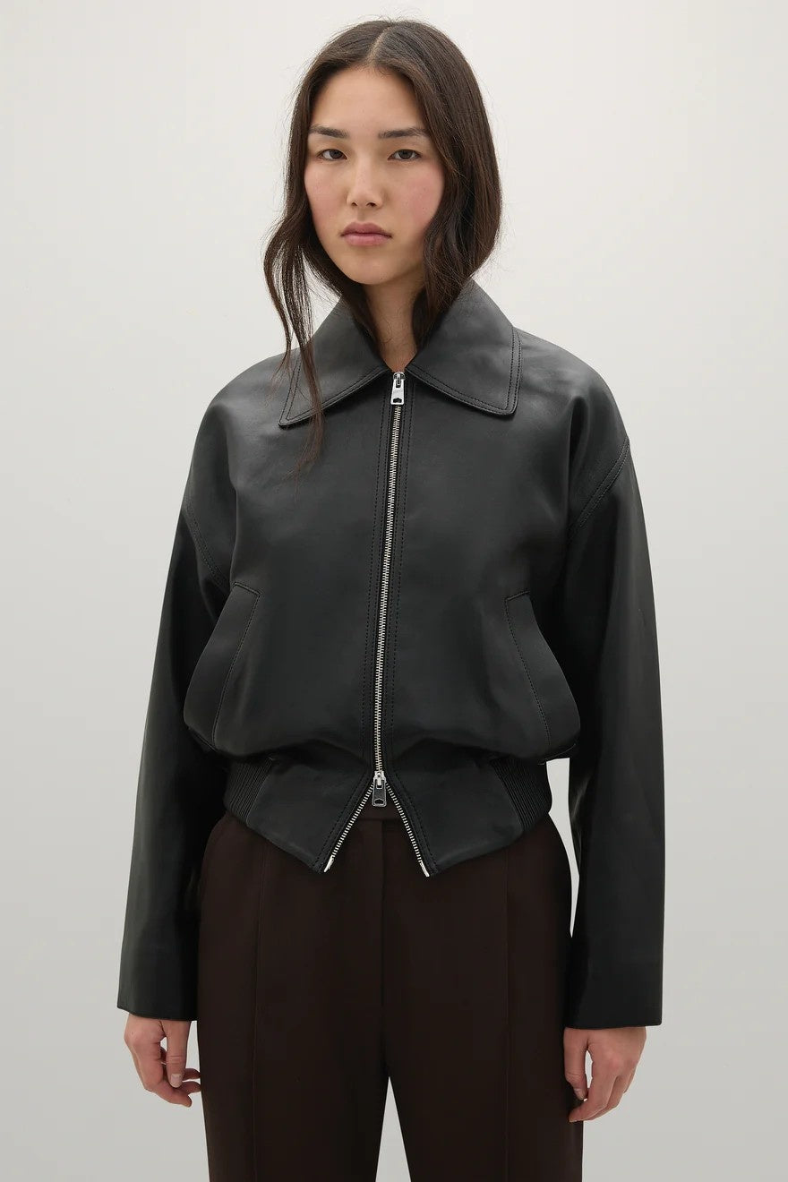 Person wearing a black leather jacket on a plain background