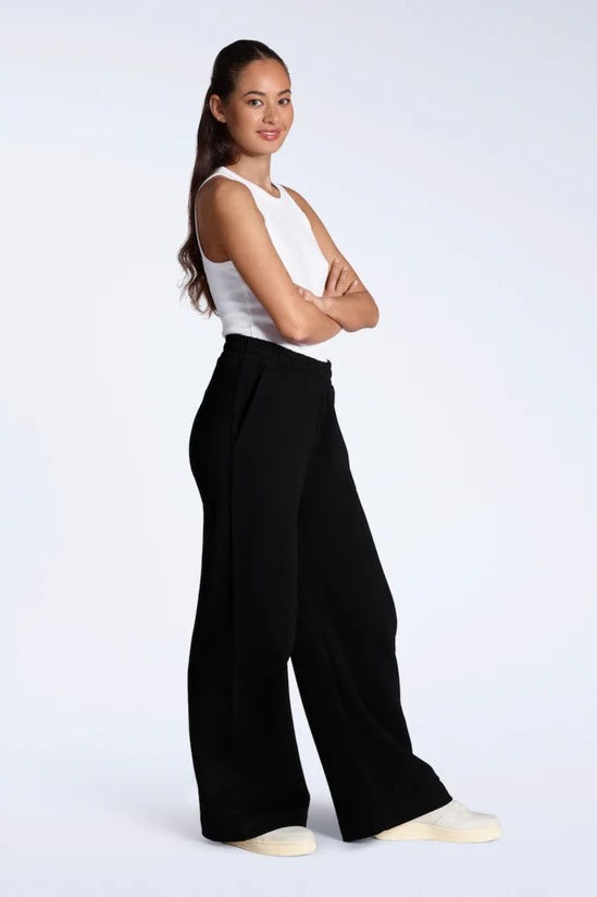 Woman wearing a white sleeveless top and black wide-leg pants on a white background
