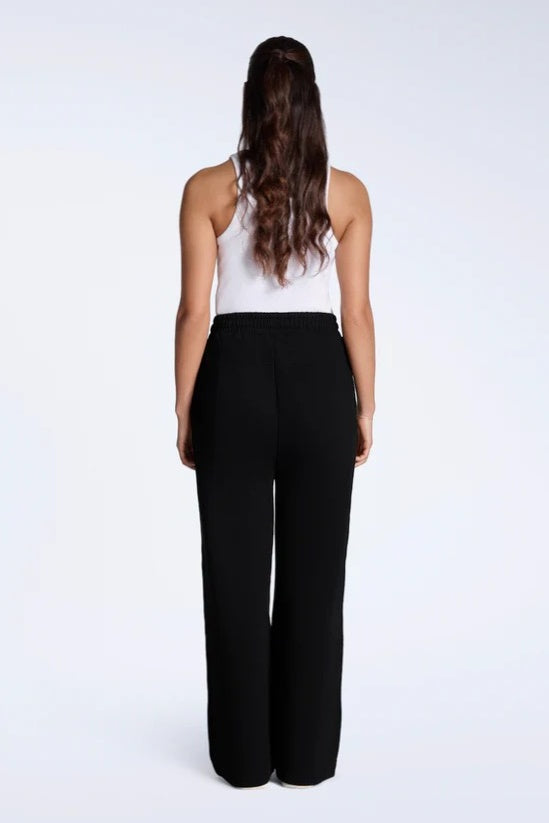 Person wearing a white sleeveless top and black high-waisted pants on a white background