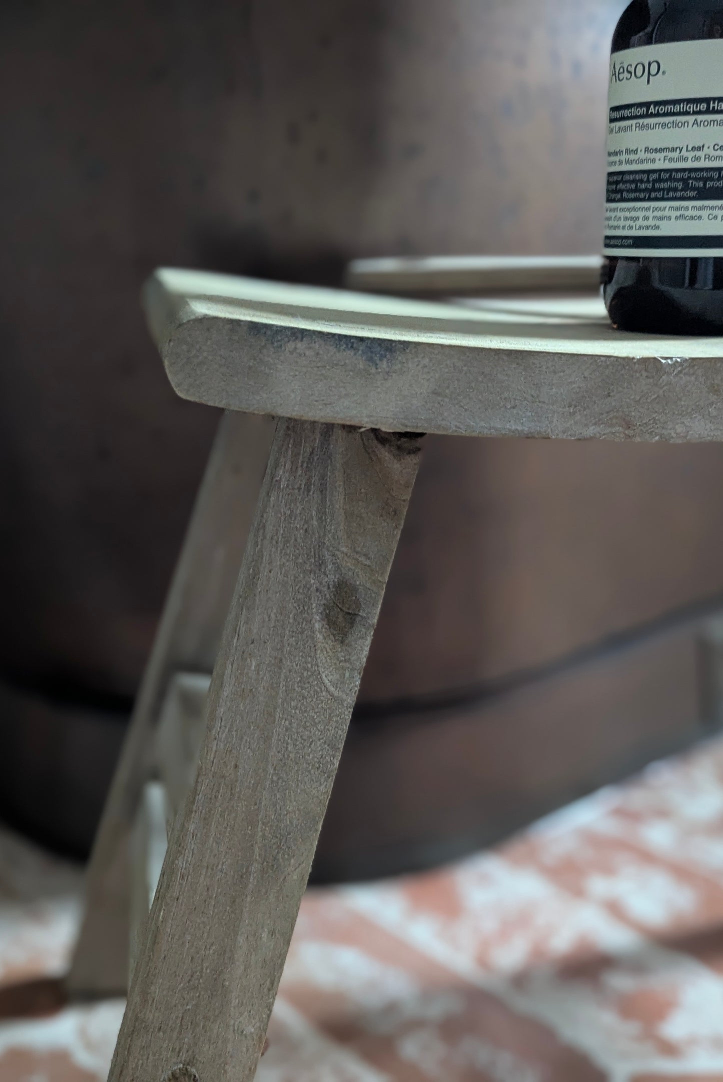 Wooden stool with a bottle of Aesop product on top, blurred background