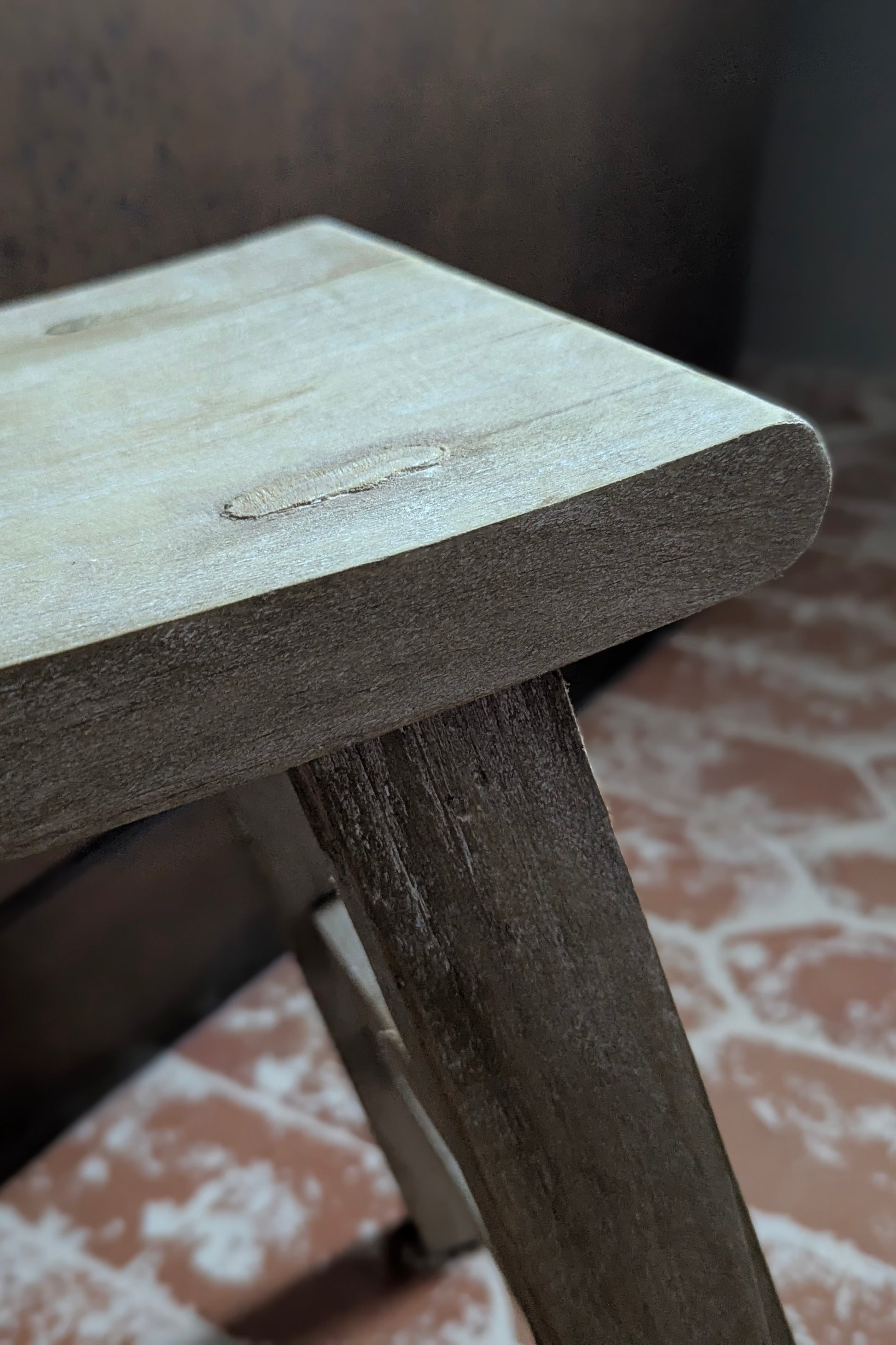 Close-up of a wooden stool with a worn surface on a patterned floor.