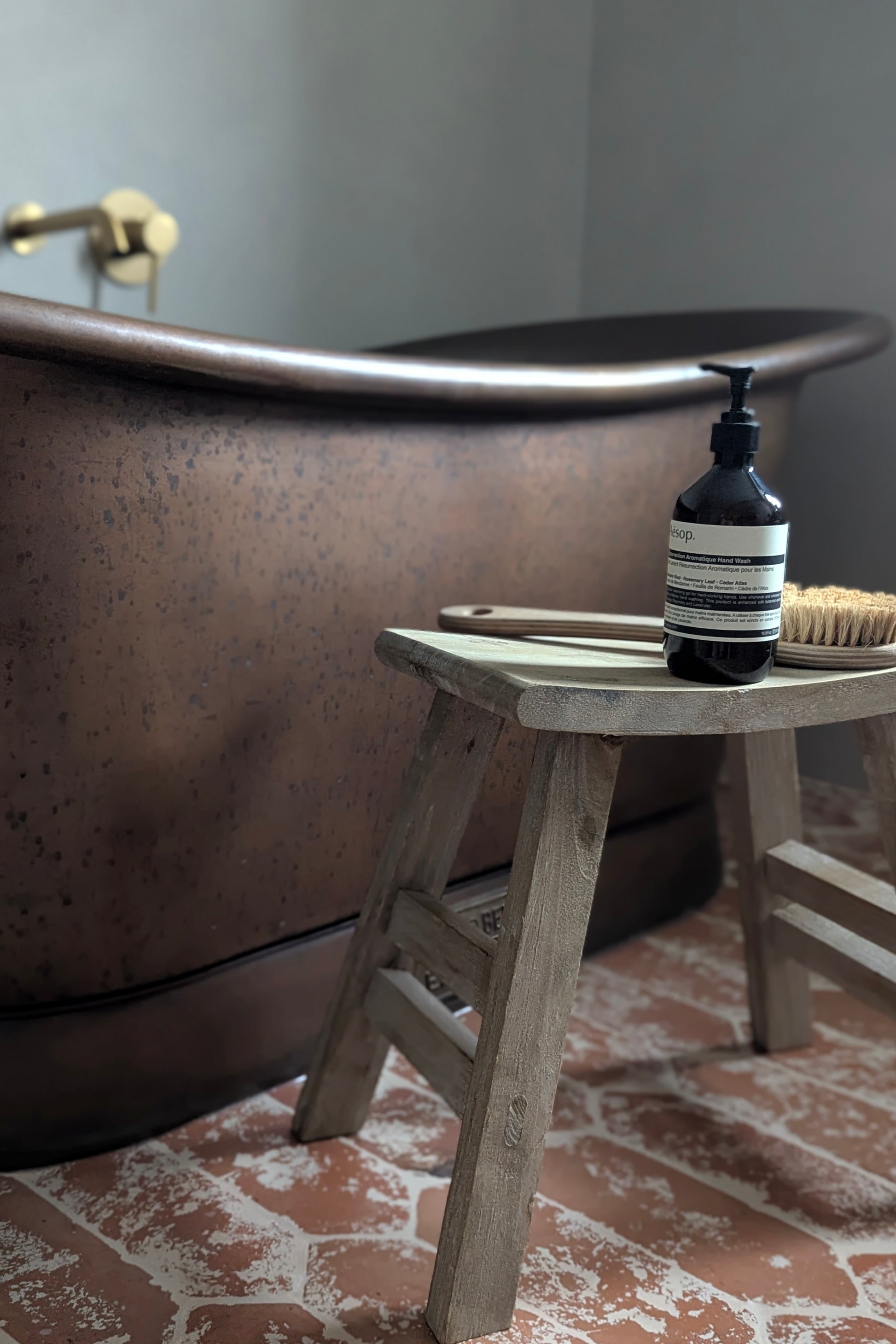 Bottle of soap on a wooden stool next to a freestanding bathtub in a bathroom.