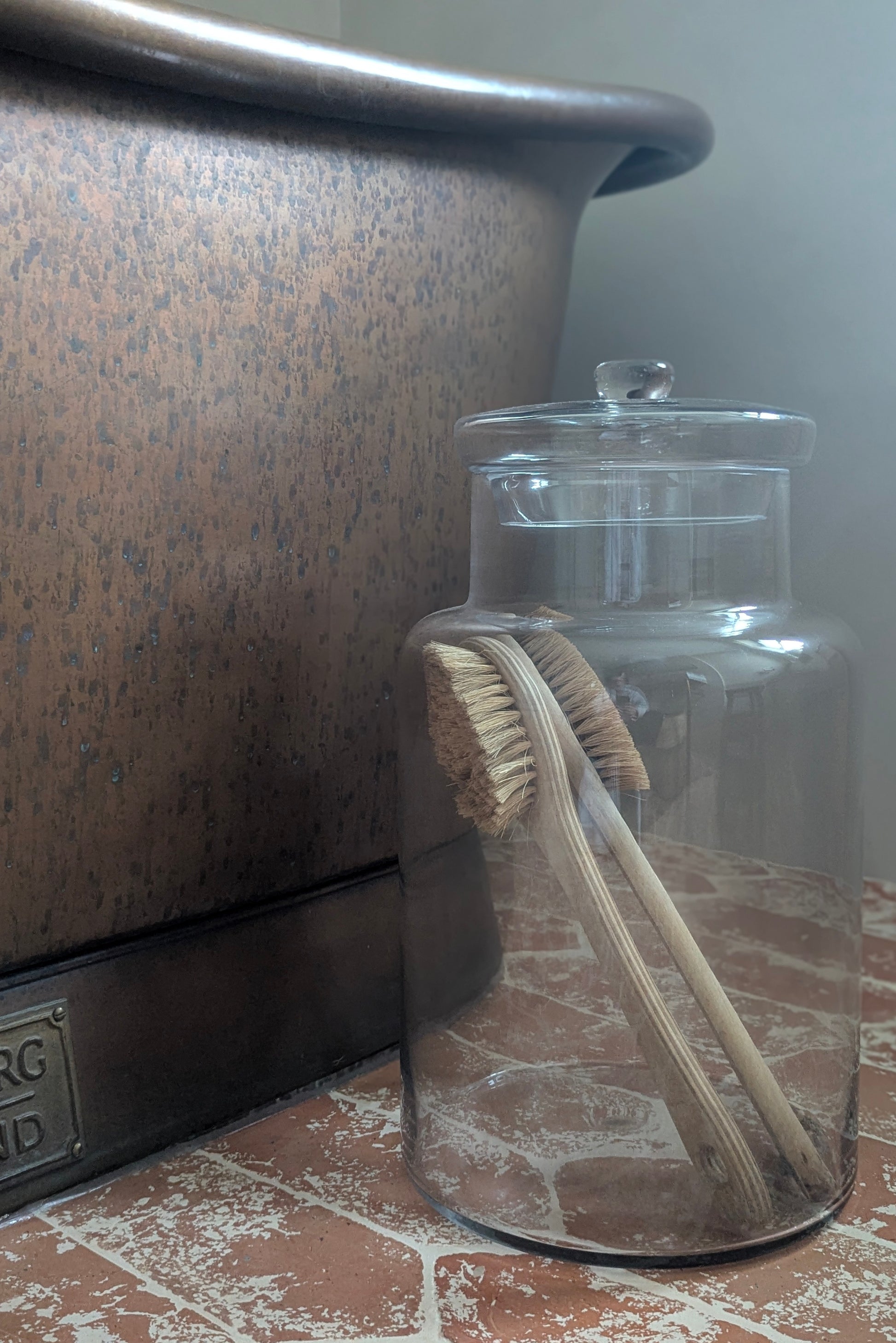 Clear glass jar with a lid containing a wooden brush on a tiled floor.