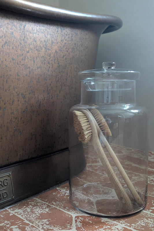 Clear glass jar with a lid containing a wooden brush on a tiled floor.