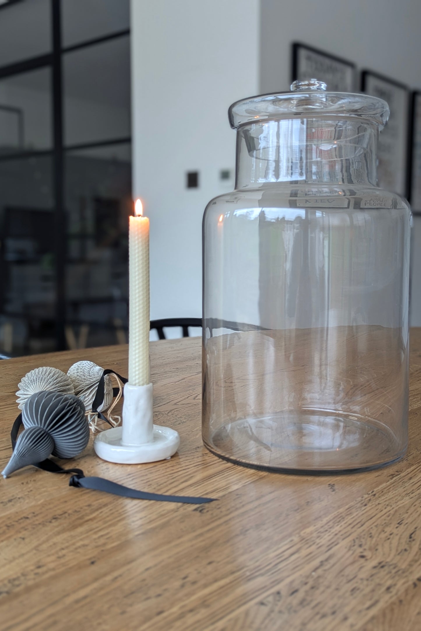 Clear glass jar on a wooden table with a lit candle and decorative items.