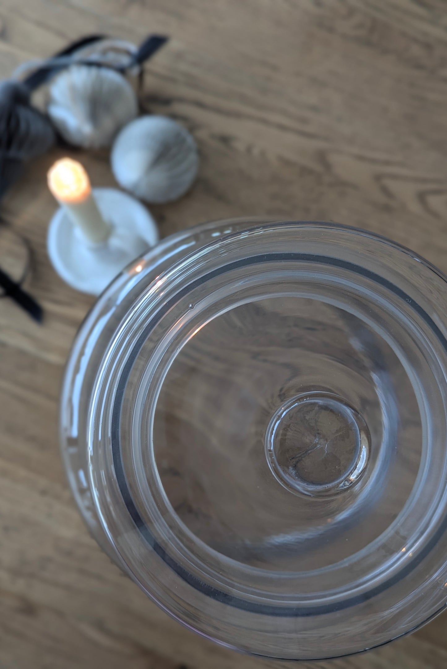 Clear glass jar on a wooden surface with a candle and decorative items in the background.